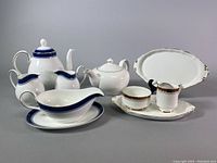 Full assortment of Royal Albert and Royal Doulton chinaware laid out including teapots, creamers, sugar bowls, gravy boat, and serving trays with gold and blue accents