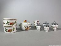 Photo displaying two ribbed casserole dishes, covered baking dish, four ramekins, and several egg coddlers with silver lids, all decorated with the Royal Worcester Evesham fruit pattern.