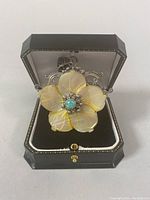 Front view of flower pendant inside a black hinged display box, showing mother of pearl petals and turquoise stone center.