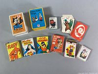 Photo showing all the card decks arranged in two rows, featuring vintage children's characters and comic figures.