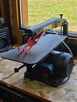 Side view of 15 inch scroll saw showing the table, arm, blade, motor base, and blade guard