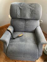 Blue fabric power lift recliner chair in upright position with remote control placed on seat.