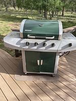 Front view of Brinkman green and silver gas grill with four burner knobs and storage cabinet.