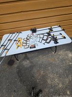 Photo of various clamps displayed on a white folding table outdoors against a wooden background