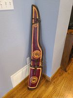 Full view of the handmade leather rifle case, showing maroon, tan, and dark brown coloring, stamped details, and securing straps.
