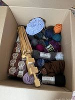 Photo showing a cardboard box containing multiple skeins of yarn in various colors and a wooden yarn winder.