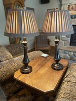 Two matching table lamps on a wooden coffee table in a living room setting, with beige pleated lamp shades turned on.