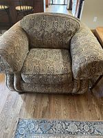 Front view of one overstuffed armchair with paisley upholstery showing seat cushion, arms, and backrest.
