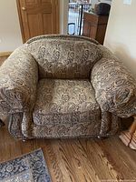 Front view of an overstuffed armchair covered in paisley patterned fabric with bulky arm protectors.