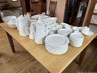 Wide view of large ceramic dinnerware set spread on wooden table including teapots, cups, and plates