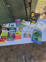 Photo showing an assortment of multiple open bags and containers of plant food and fertilizer laid out on a white surface outside near a shed.