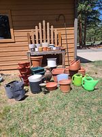 Photo showing wooden potting bench with multiple plant pots in ceramic, plastic and fabric around it including 2 watering cans