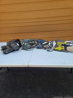 Four power sanders on a white table against a brown wall background, showing various colors and brands.