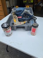 Ryobi biscuit jointer with two containers of Porter Cable biscuits on white table with gray carrying case in background