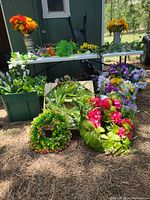 Photo of various silk flowers, vines, and wreaths displayed outdoors on a white table and ground in front of a green shed