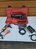 Four electric cutting and engraving tools arranged on a table. Includes red angle grinder, black engraving tool in red case, black and red jig saw, and black spiral saw. Also includes charging/base unit.