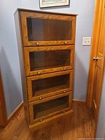 Tall wooden barrister cabinet with four tilt-up, slide-in glass doors.