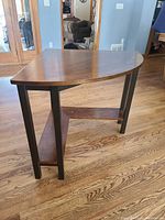 Brown wooden corner table with lower shelf, measuring 32 inches by 32 inches, in a room with hardwood floors.