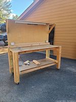 Full view of the wooden workbench placed outdoors next to a building, showing peg board, lower shelf, wheels, and light.