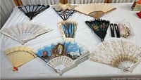 Overview of 12 decorative hand fans of varying styles and colors, laid out on a white surface.