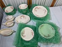 Full view of the china set arranged on a table showing stacks of plates, bowls, saucers, and individual serving pieces wrapped in green bubble wrap.