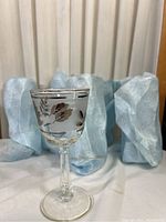 Single clear tall glass featuring a chrome-colored leaf decoration around the bowl, displayed wrapped individually