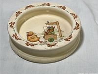 Side angle of the round dish showing rabbit border and bunny/chick design inside.