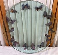 Full view of round thick glass dish with butterfly edges against a white curtain background.