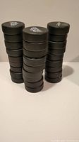 Three stacks of black hockey pucks, stacked on a surface, showing multiple pucks with numeric markings on one side.