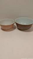 Two vintage Pyrex Woodlands bowls side by side, one tan and one dark brown.