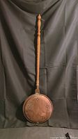 Full view of antique Victorian copper bed warmer with hinged lid and wooden handle, against black backdrop.