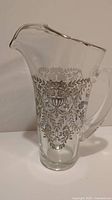 Front view of clear glass pitcher with silver floral overlay decoration covering upper half