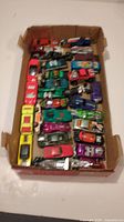 Top view of a box containing 27 brightly colored diecast Hot Wheels cars in a variety of styles and colors, arranged neatly in rows.
