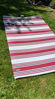 Full view of the striped outdoor mat laid flat on grass showing length and strap detail.