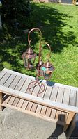 Copper finish lantern style candle holder with two hanging lanterns on a tall stand, wooden surface and grassy background