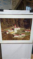 Framed photo of the Carmanah Point Lighthouse showing the lighthouse, multiple adjacent buildings, and surrounding forested area.