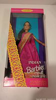 Full front view of Indian Barbie in box showing pink and purple patterned packaging, doll dressed in bright pink saree with gold border detail, visible face and accessories.