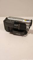 Side view of silver and black JVC VHS camcorder showing the eyepiece viewfinder and hand strap with JVC logo.