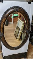 Full view of the large oval antique mirror showing beveled glass and wood grain frame with decorative elements.