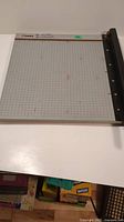 Top view of DAHLE paper cutter showing grid surface with red marking, measurement labels, and cutting arm on the right.