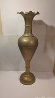 Full view of a tall vintage brass vase with ruffled top and bulbous body.