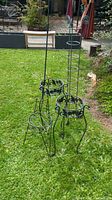 Photo showing three black metal plant stands and one tall hanging plant holder on lawn.
