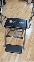 Front view of the Pilates Pro Chair showing cushioned seat and handles on a wood floor.