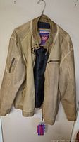 Beige leather jacket hanging on a hanger showing front and open lining.