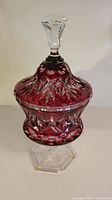 Full view of the red crystal lidded candy dish featuring a clear handle and hexagonal clear base.
