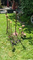 Photo showing multiple rusted garden metal plant stands, including tall stands and shorter tiered stands on grass.