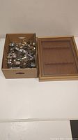 Photo of a cardboard box filled with many old collectible souvenir spoons and the display case beside it.
