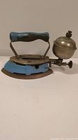 Side view of vintage Coleman Instant-Lite Model 4A gas iron showing blue body, wooden handle, metal base, and fuel tank