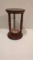Full view of the vintage wooden hourglass showing base, top, and four pillars with the glass sand timer in the middle.
