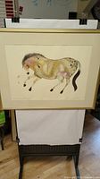 Full view of the framed artwork showing the horse and the artist's signature, along with the frame and matting.